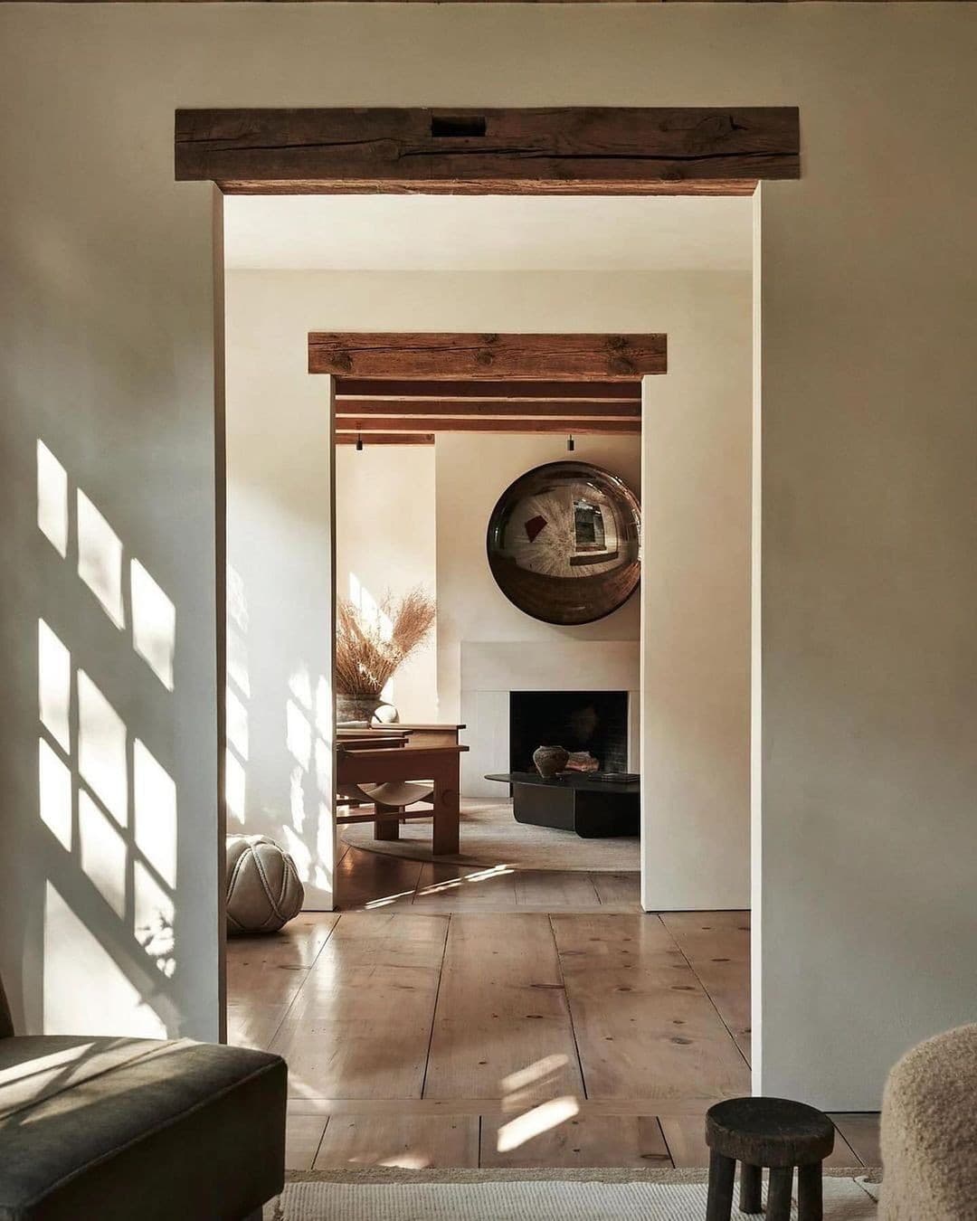 Wabi-sabi living room with exposed beams, large mushroom mirror, plaster fireplace