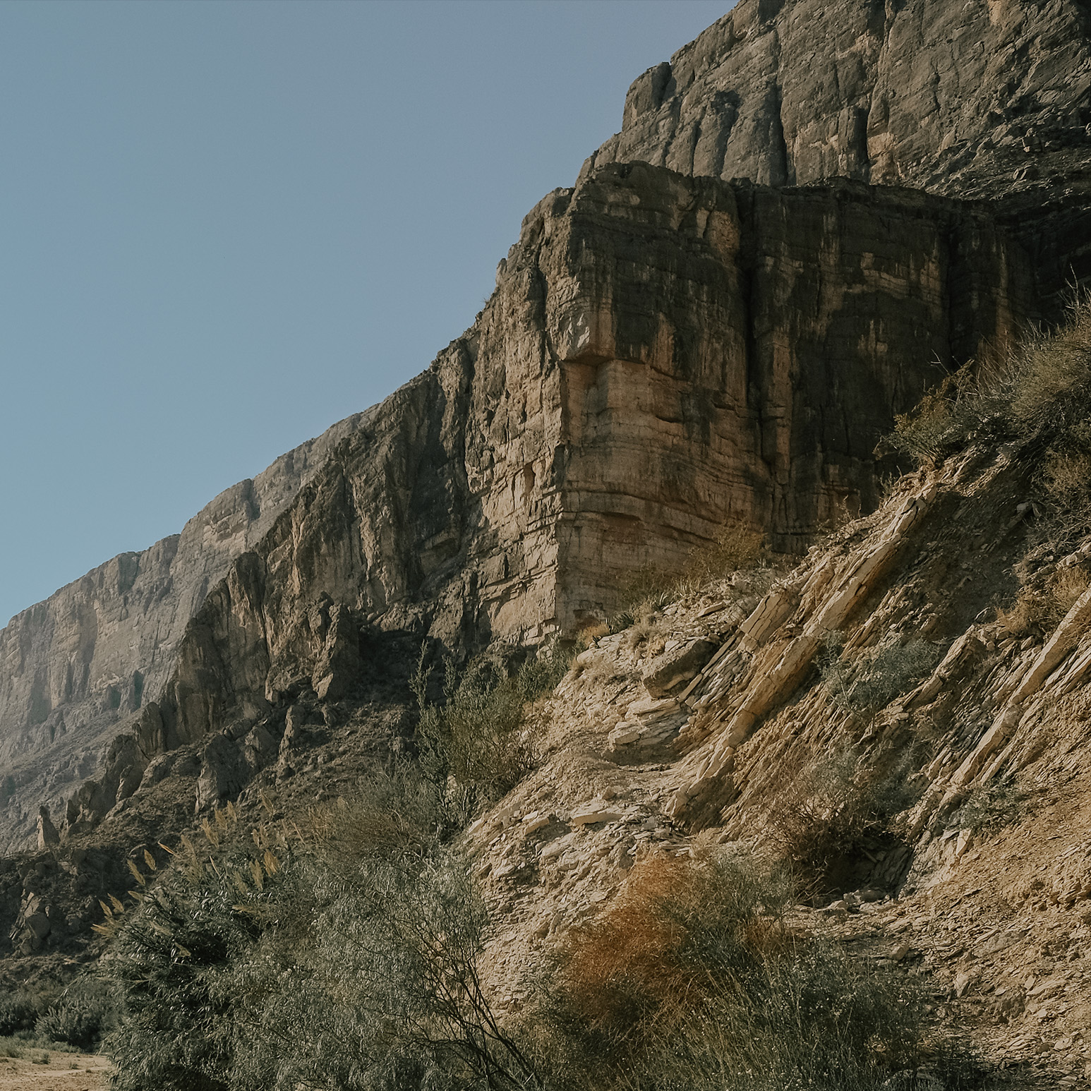 A steep canyon wall of layered rock rising straight from the desert floor in Big Bend