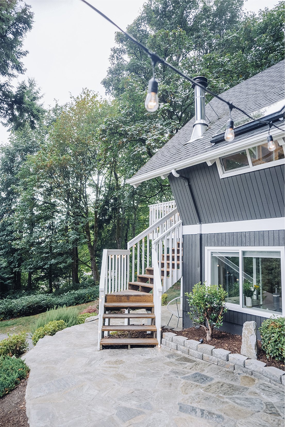 Back-side view of the chalet showing the deck overhang, white-railed staircase down to a stone patio, and the landscaped garden line