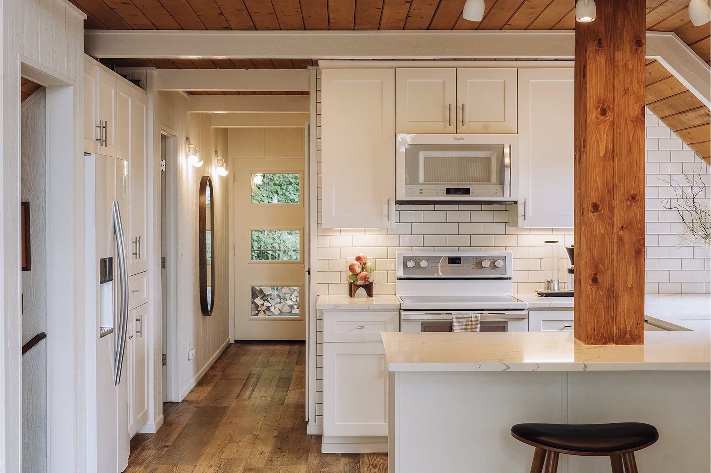 Chalet kitchen with white shaker cabinets, subway tile backsplash, an exposed wood beam column, and PNW pine floors