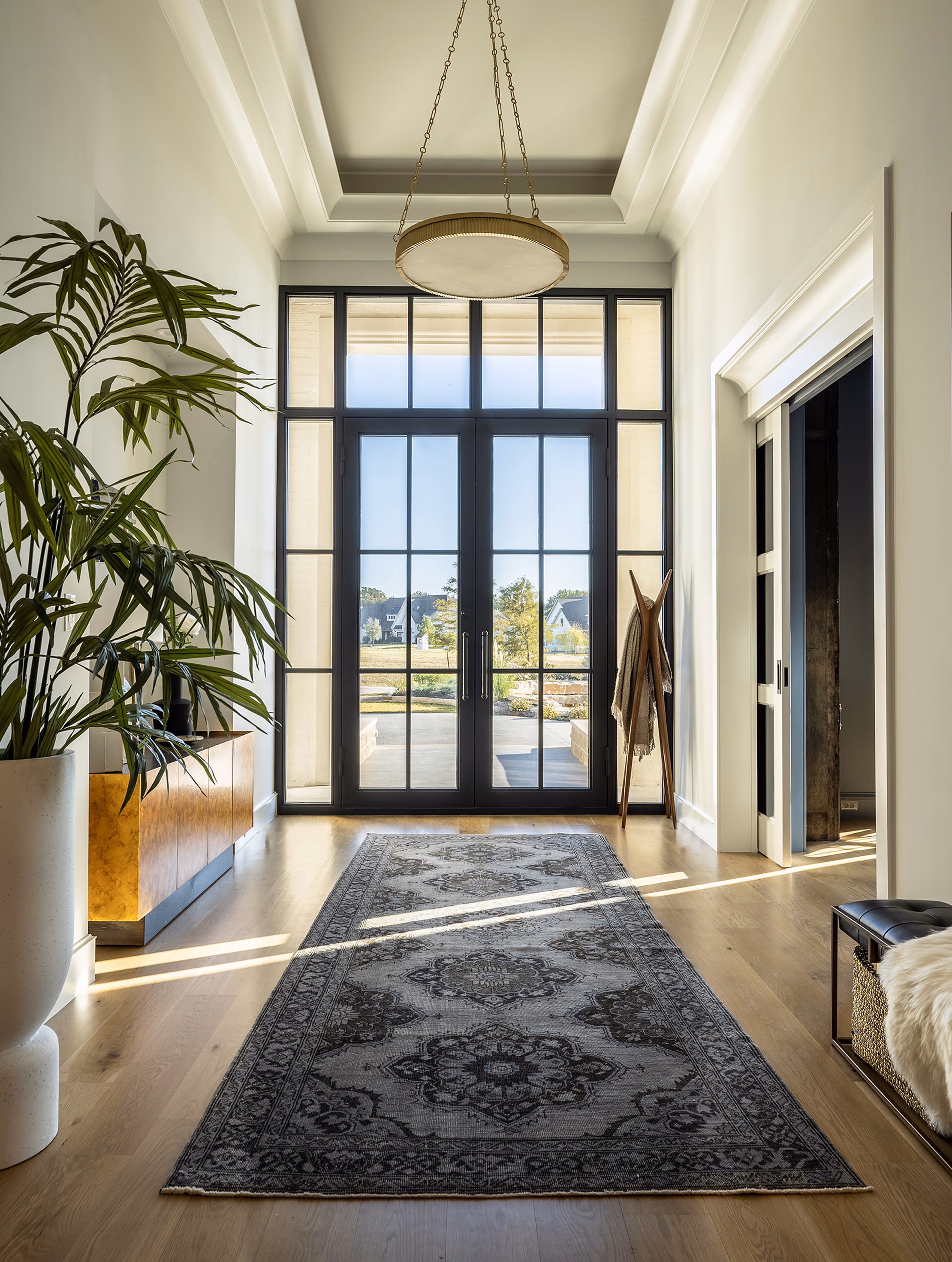 Vertical view straight through the foyer to the French doors with the brass chandelier overhead and the full vintage rug runner anchoring the floor