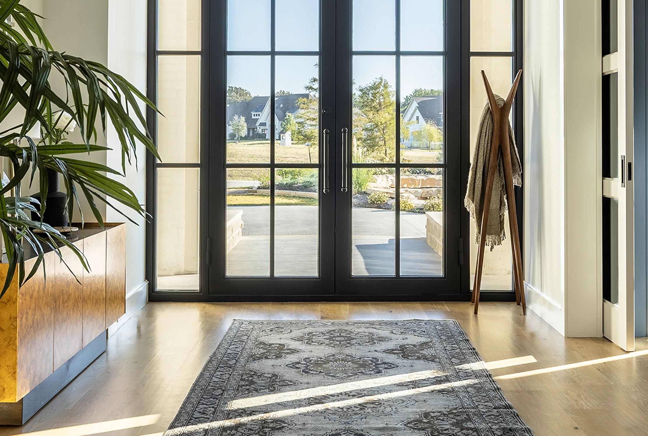 Horizontal architectural view of the entry: French doors at center, vintage rug runner, palm on the left, coat tree against the side wall