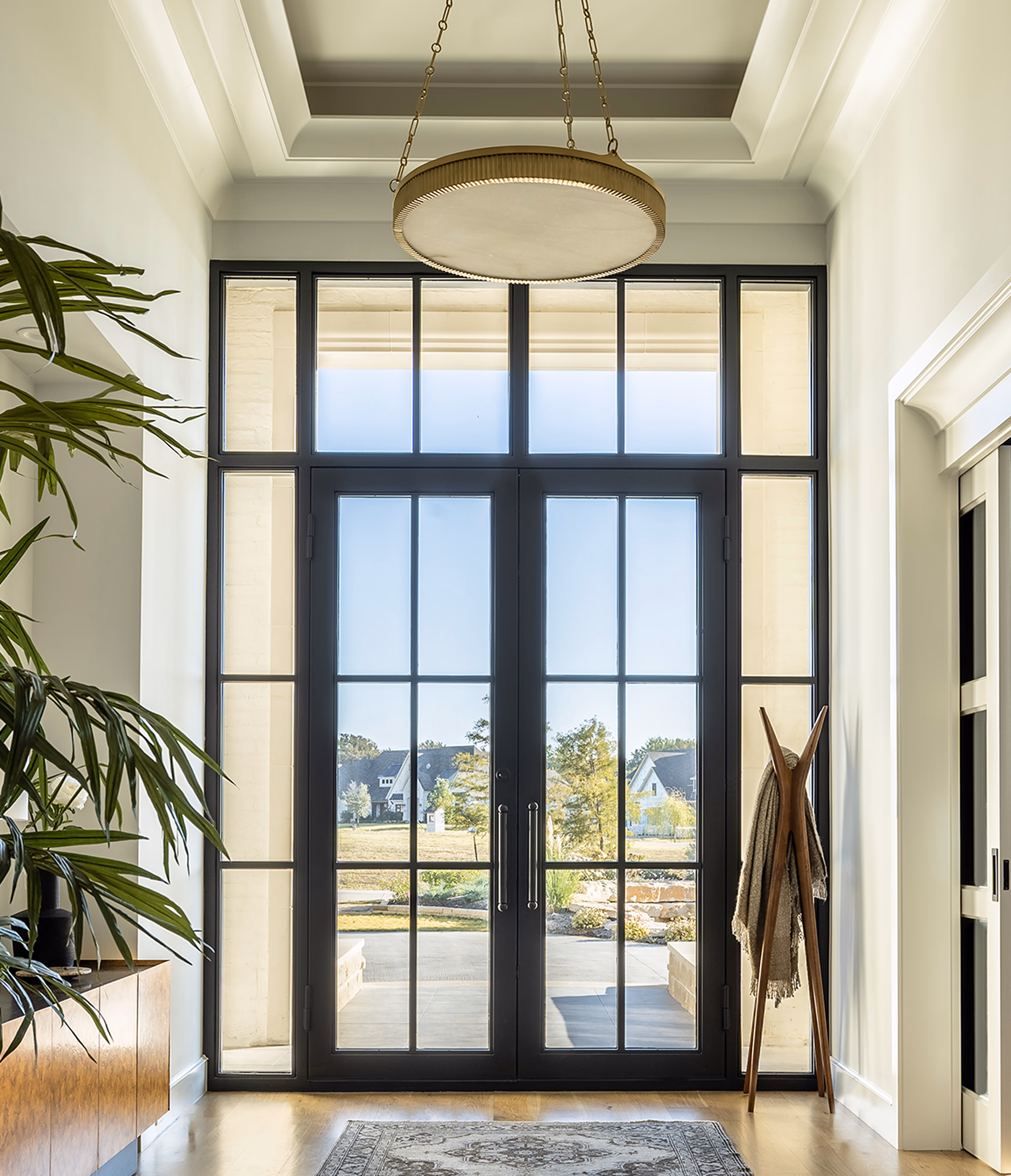 Vertical composition looking up at the brass and alabaster chandelier with French double doors and transom windows running the full two-story height
