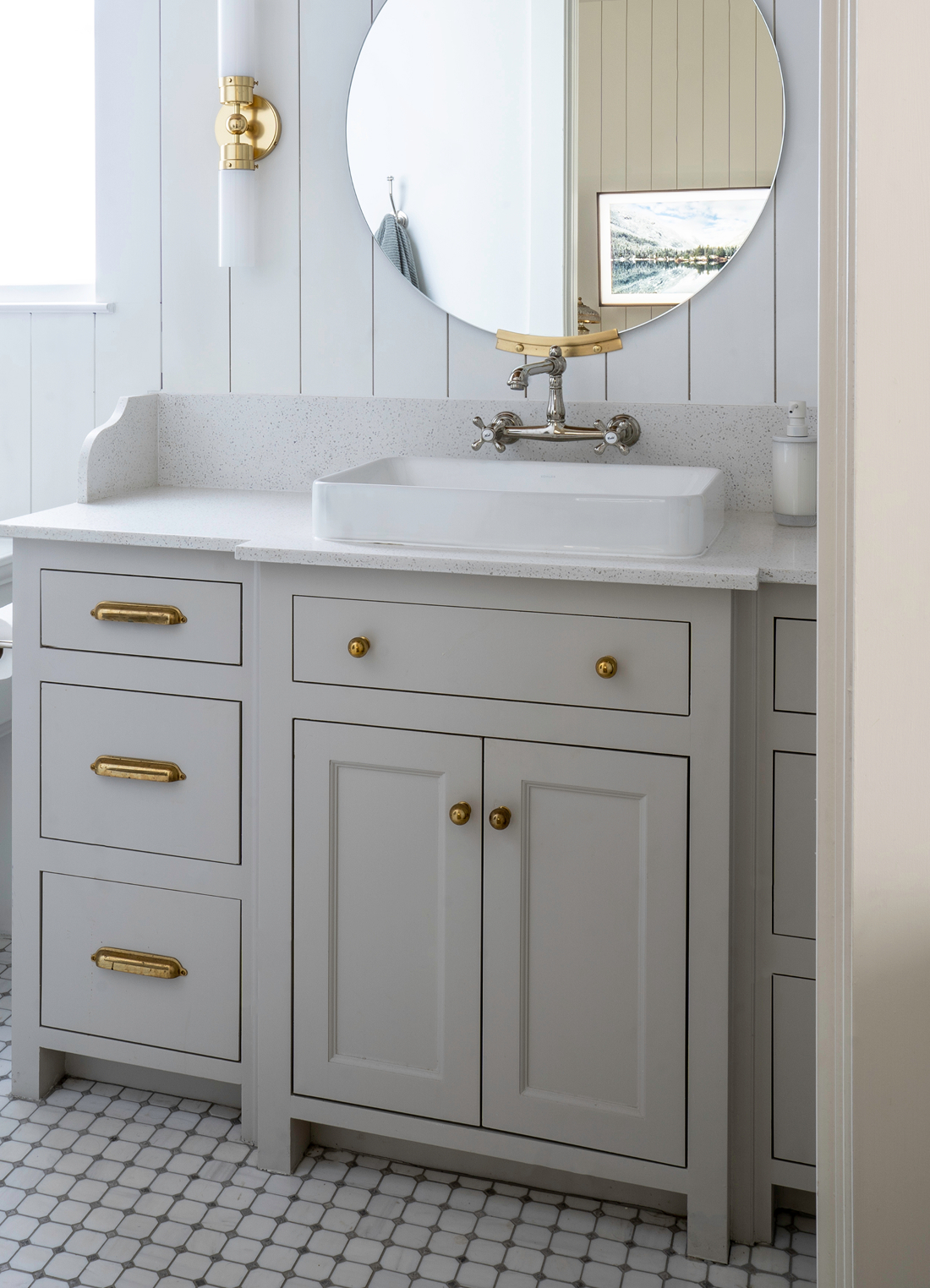 Modern farmhouse powder room with circular brass mirror, brass cabinet pulls, brass sconce, vessel sink, and patterned hex floor tile
