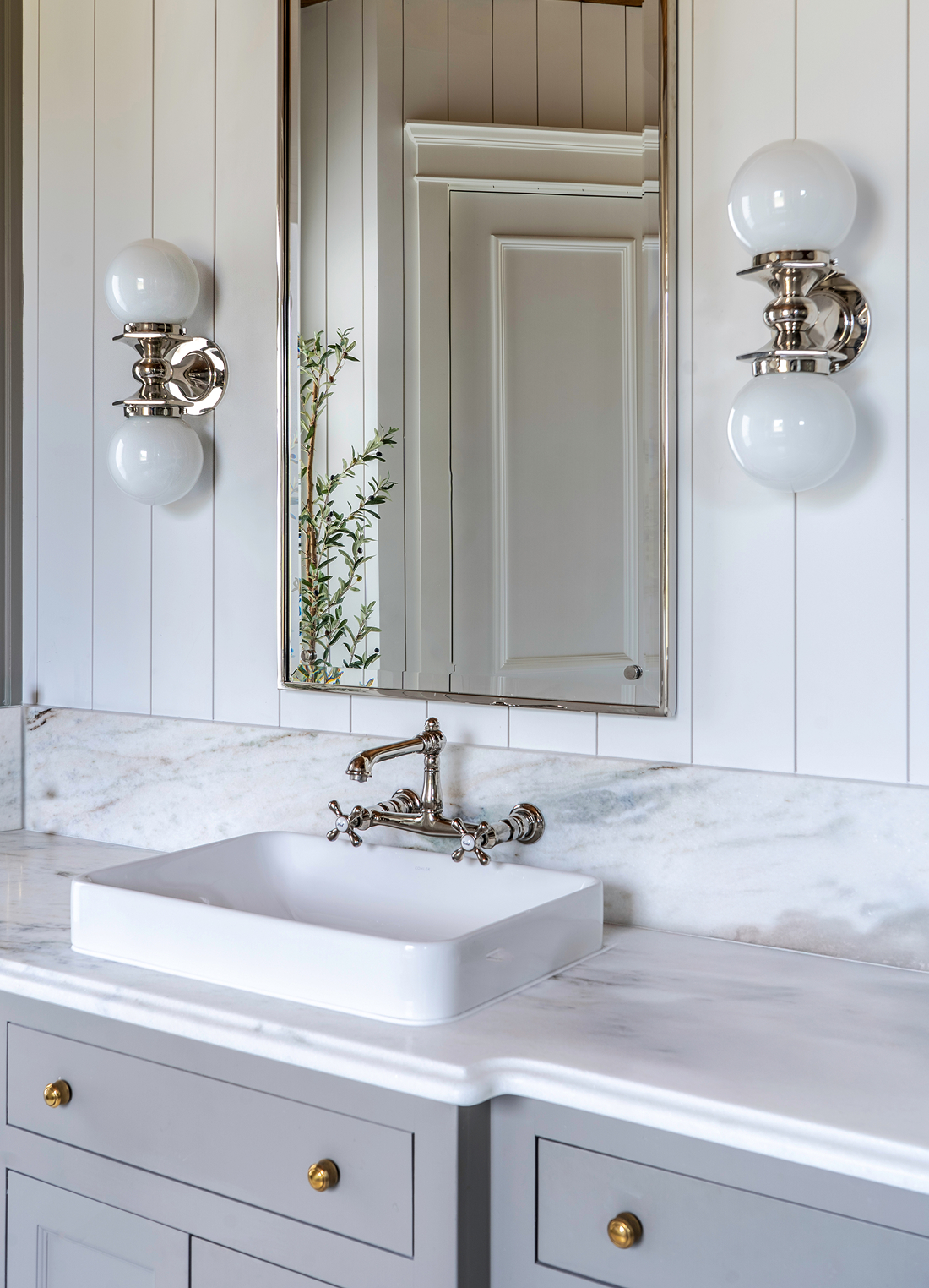 Modern farmhouse vanity detail with vertical shiplap, veined marble counter, polished nickel sconces with milk glass globes, vessel sink, and brass mirror