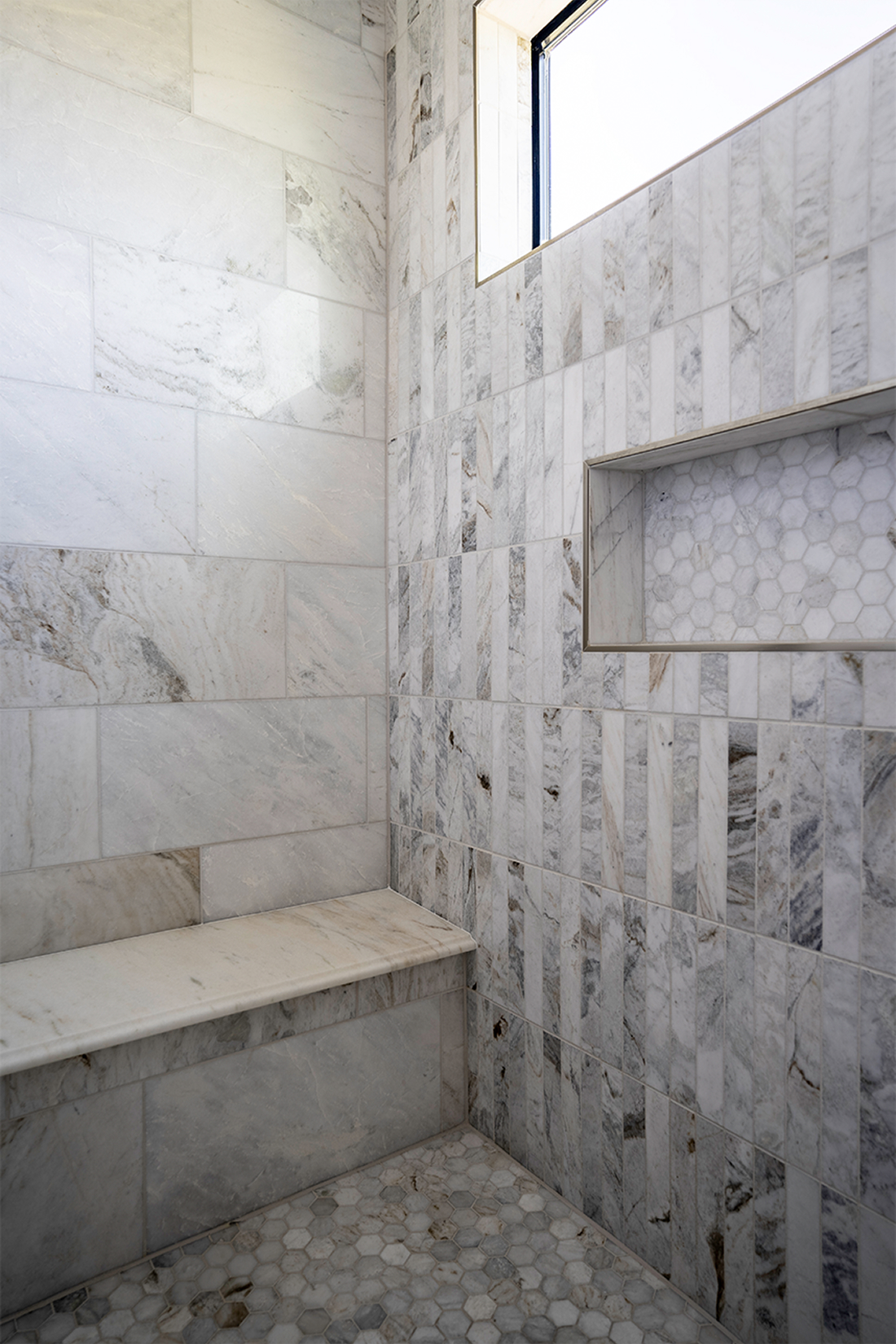 Urban southwest marble shower with vertical stacked tile, recessed niche with hexagon detail, marble bench, and clerestory window
