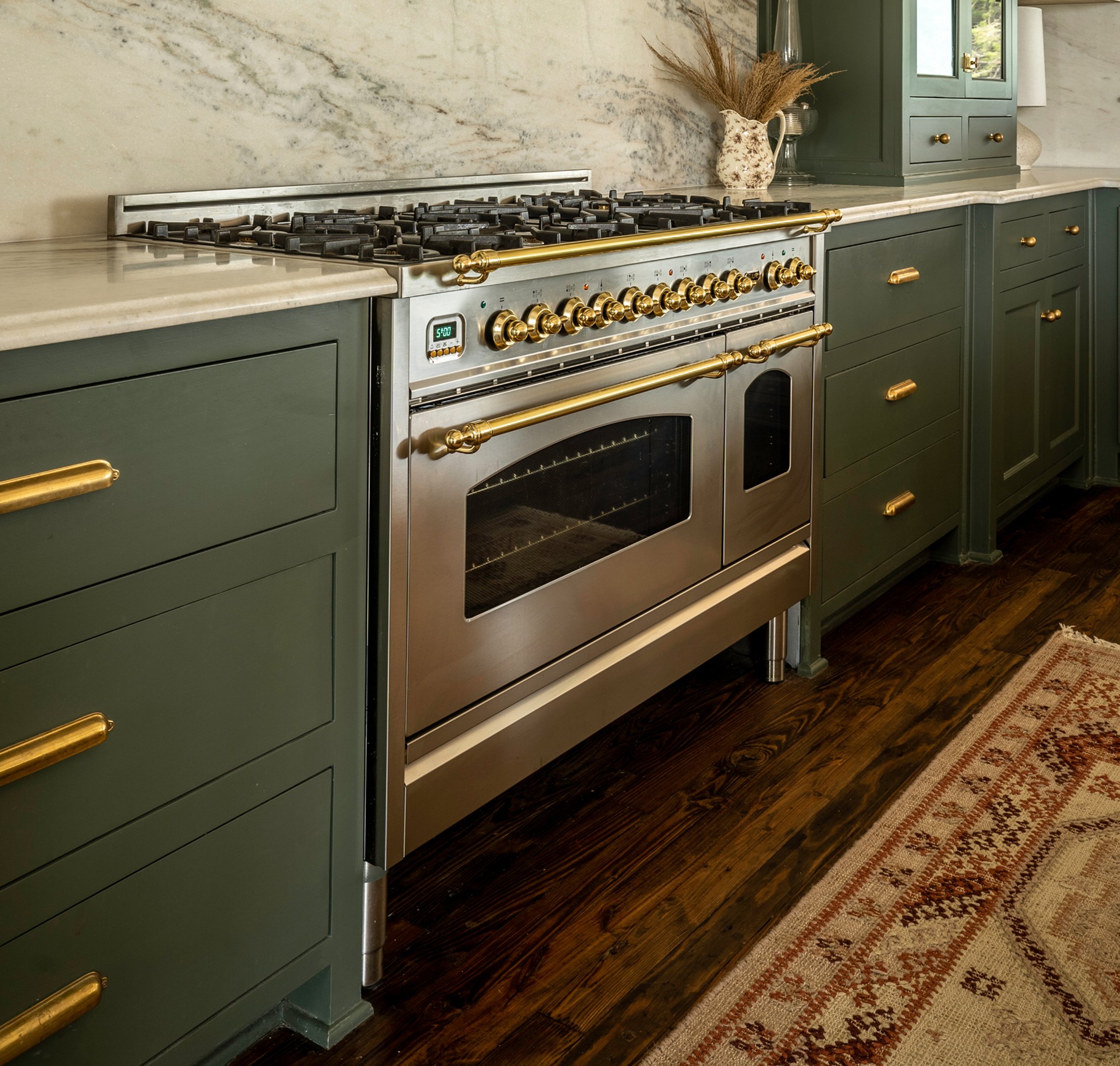 Professional range with brass knobs, marble backsplash, sage green cabinetry