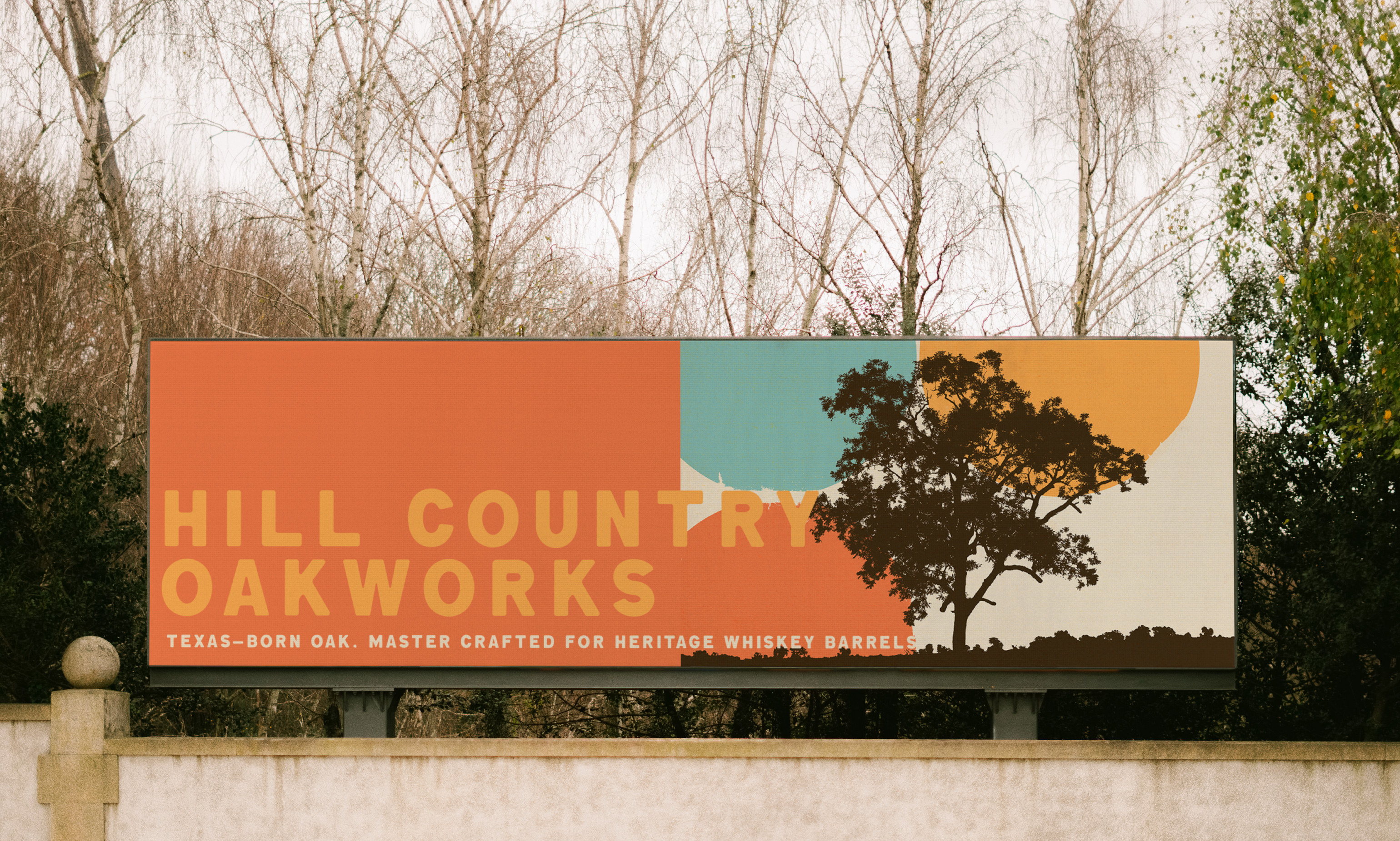 The Hill Country Oakworks billboard standing against bare winter trees, the tree silhouette and colour blocks running the full width