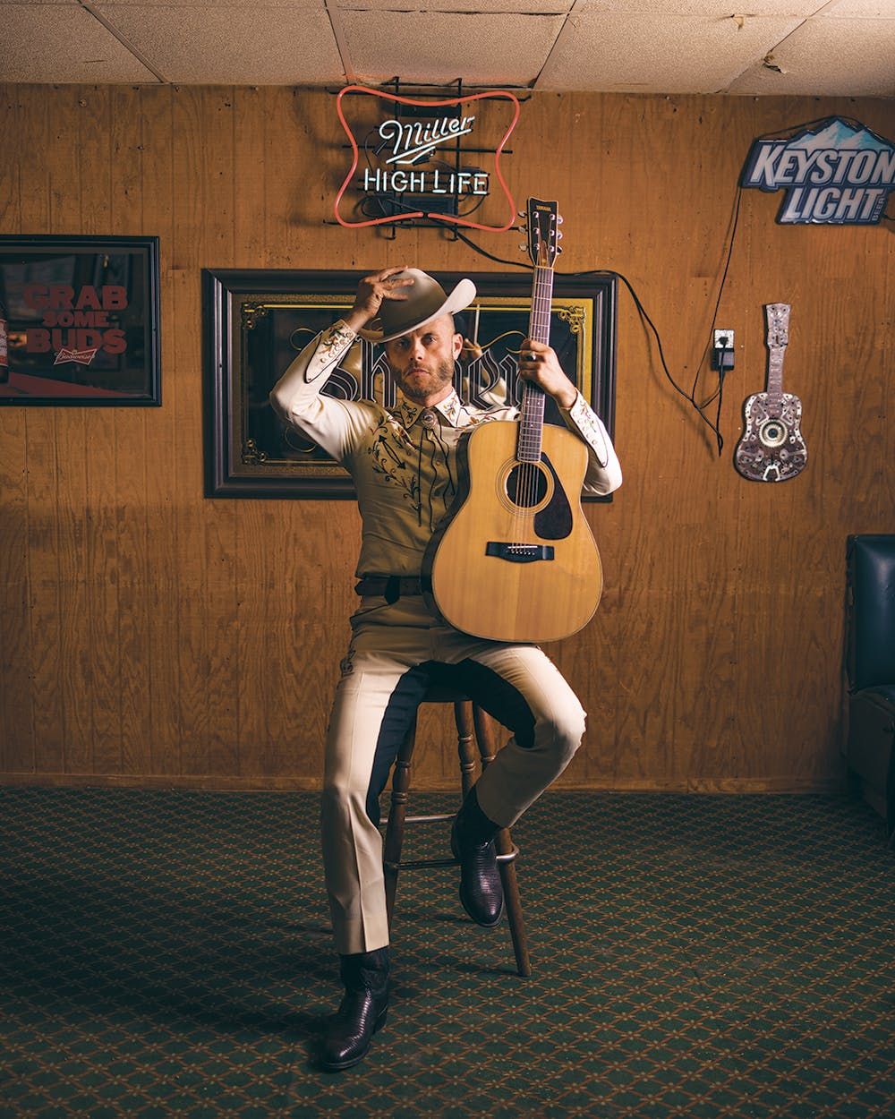 Country singer in cowboy hat with acoustic guitar, Miller High Life neon sign behind