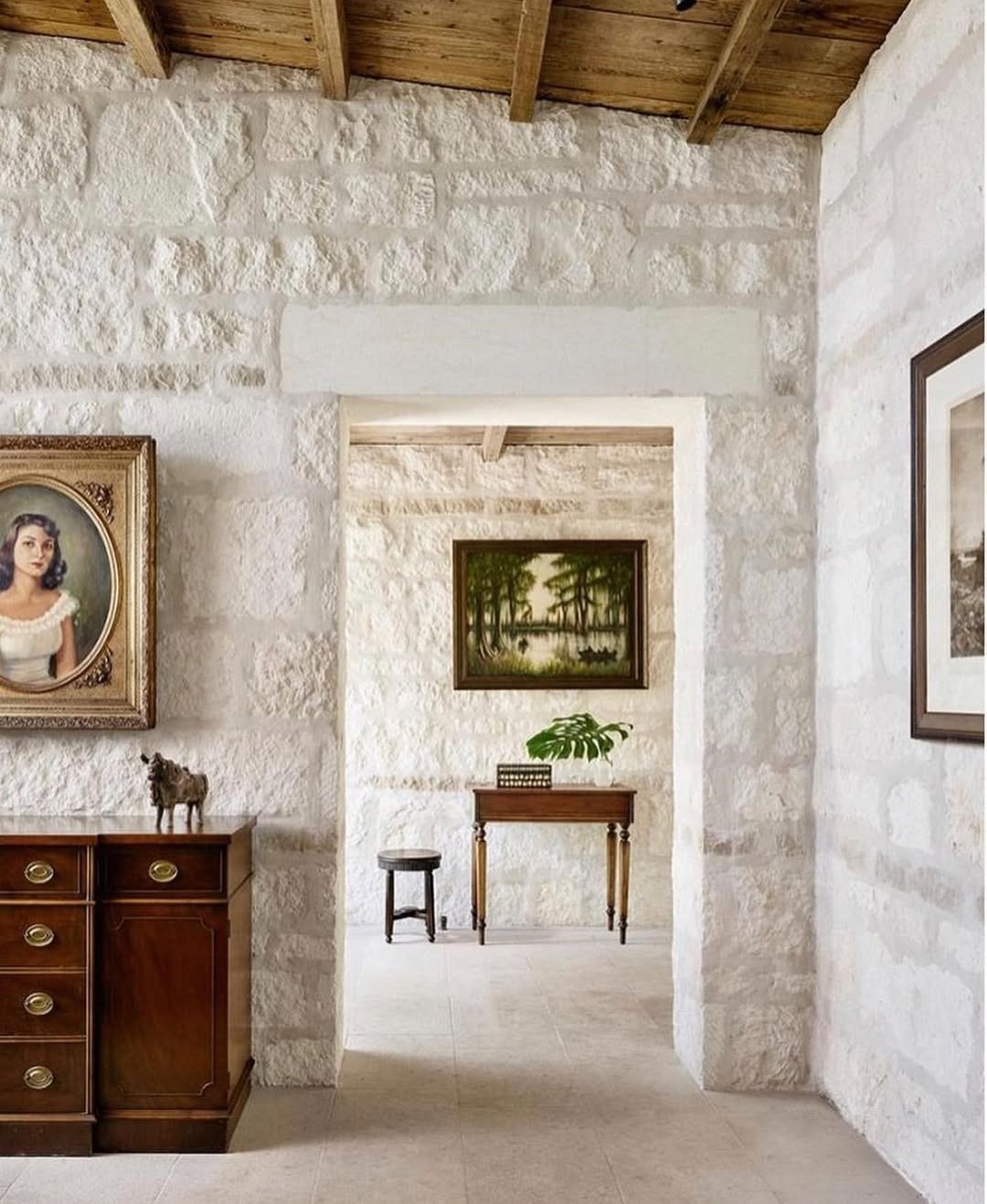 Texas Hill Country stone foyer with antique portrait, dark wood console, and a monstera leaf