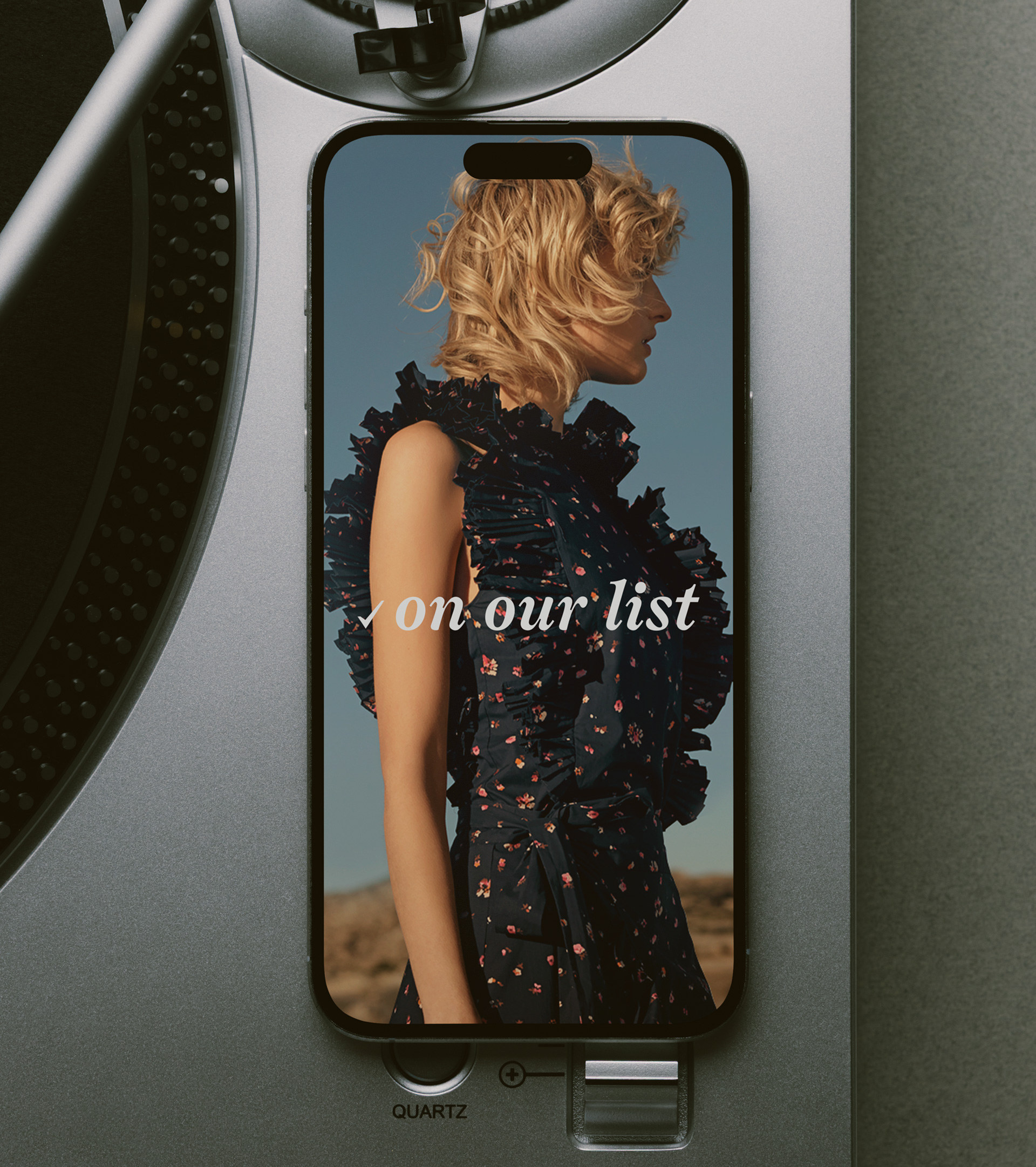 A phone lying on a silver turntable showing the On Our List story, the bucket's script lockup over the editorial photograph