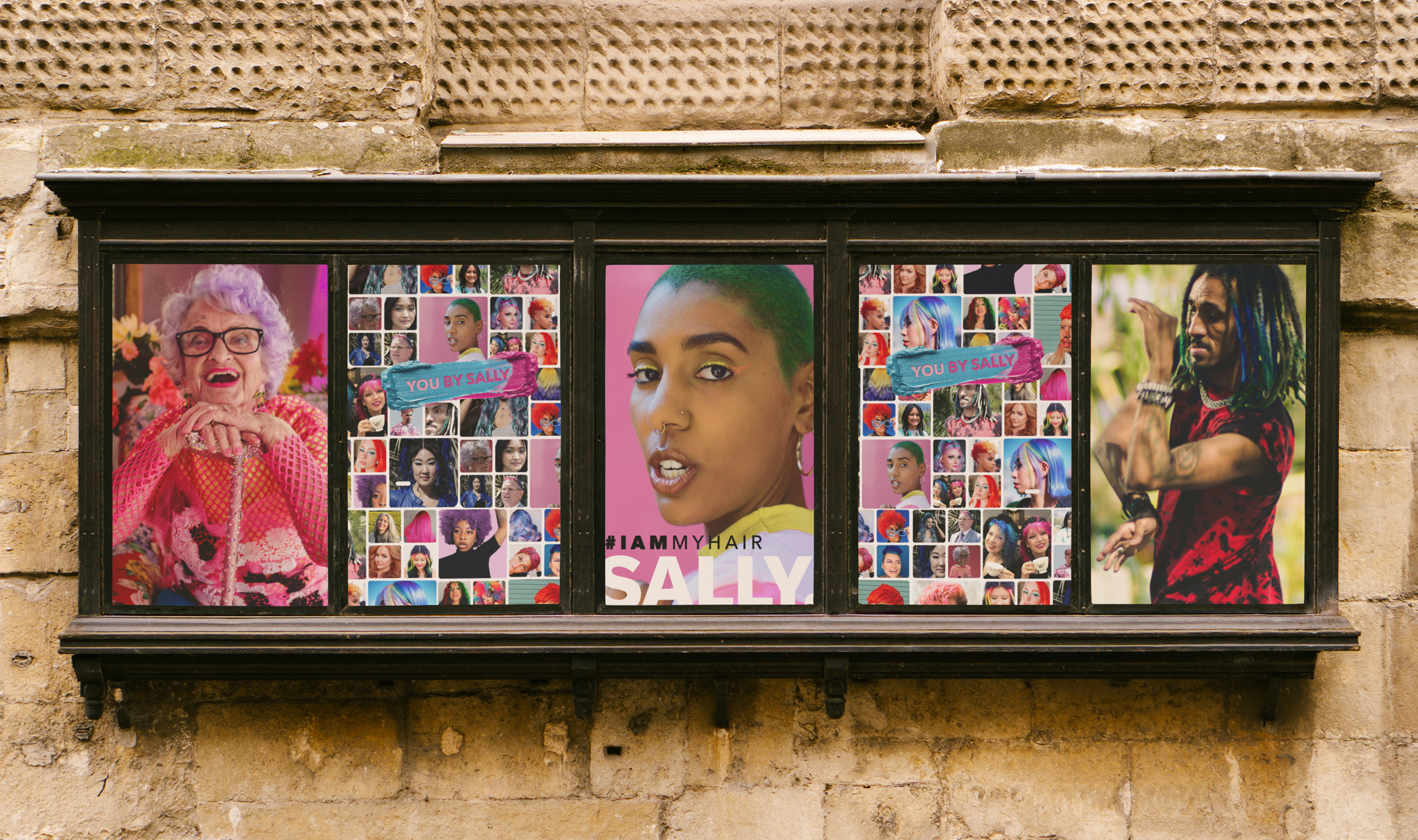 The You By Sally campaign in a five-panel street display case on a stone wall, portraits either side of the mosaic and the I AM MY HAIR panel